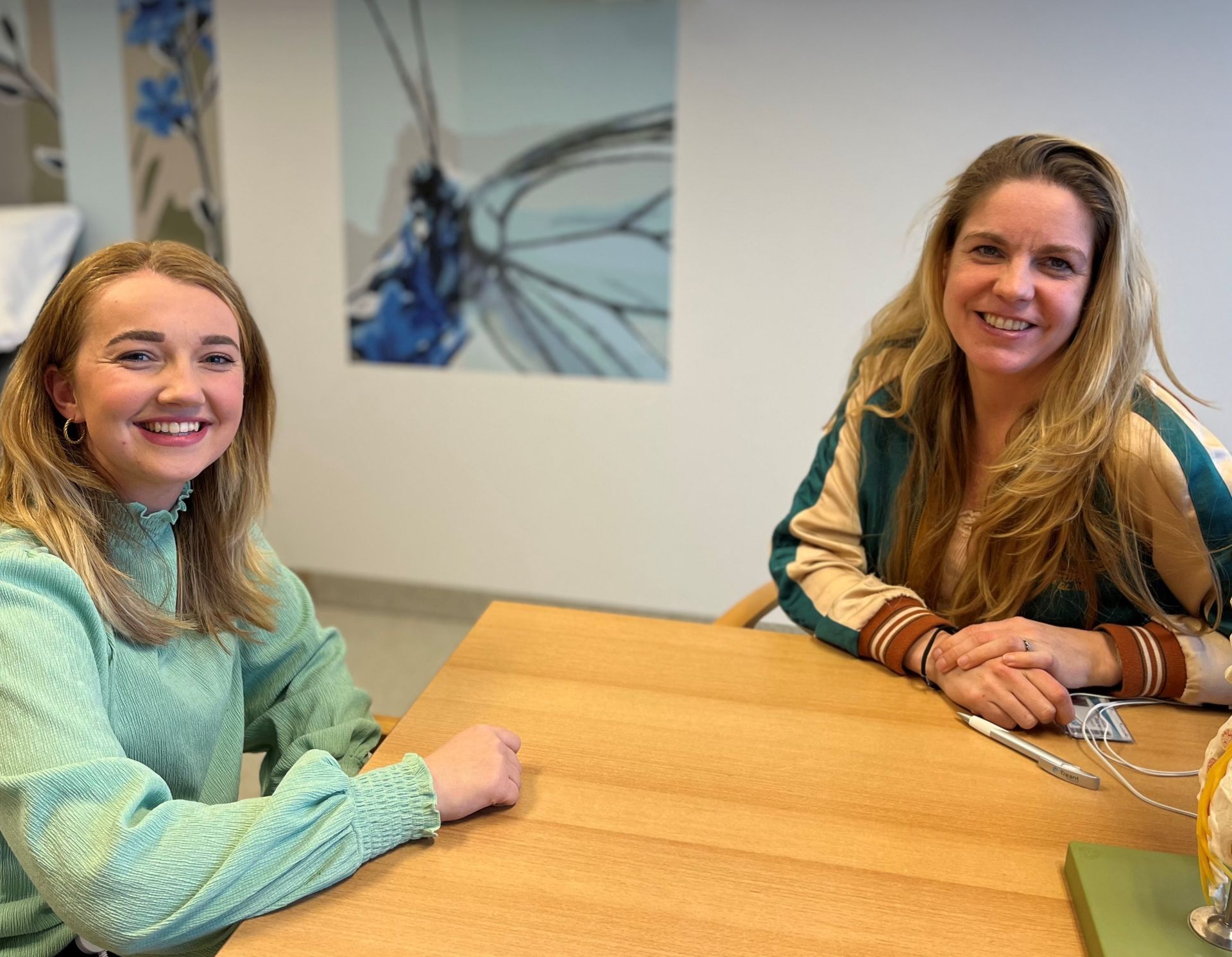 Verpleegkundigen Selina en Wietske zitten in de spreekkamer van Wietske aan tafel.