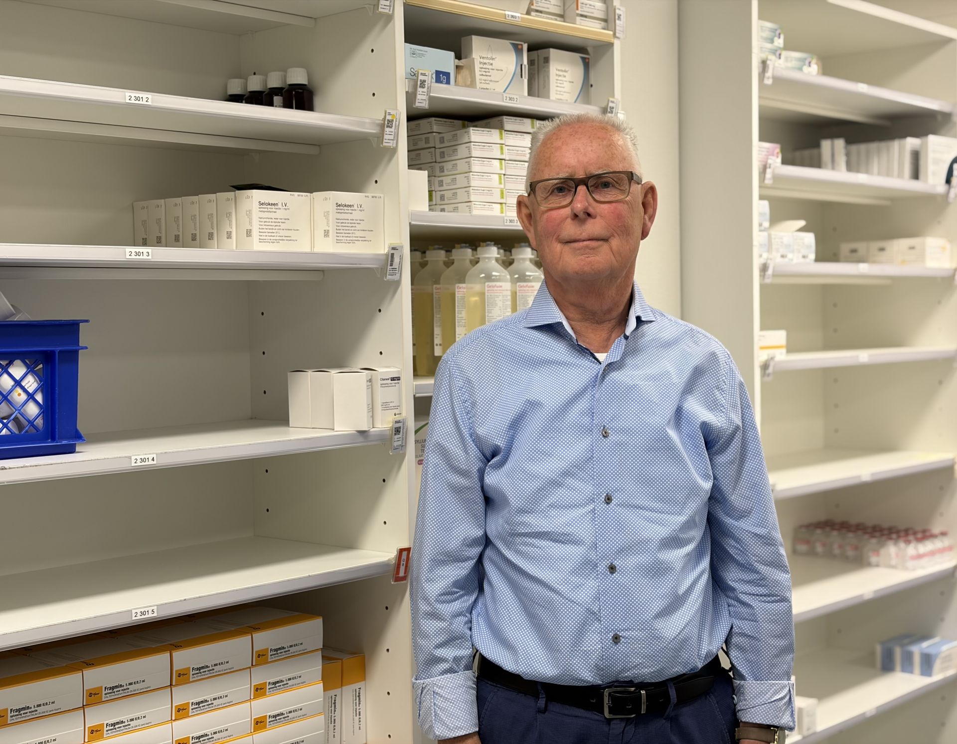 Een man in een apotheek met schappen vol medicijnen.