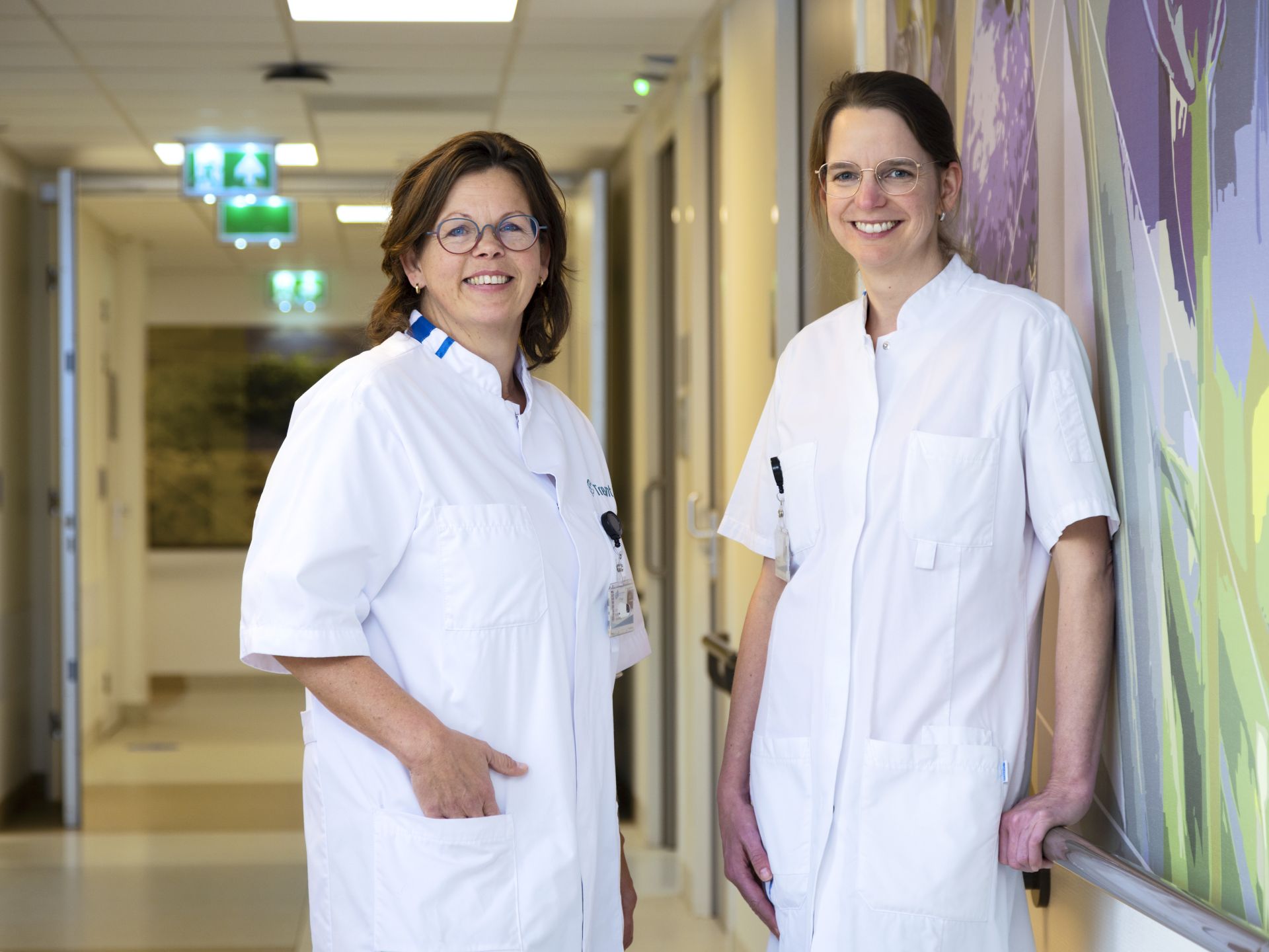 Twee vrouwelijke artsen glimlachen in de gang van een ziekenhuis.