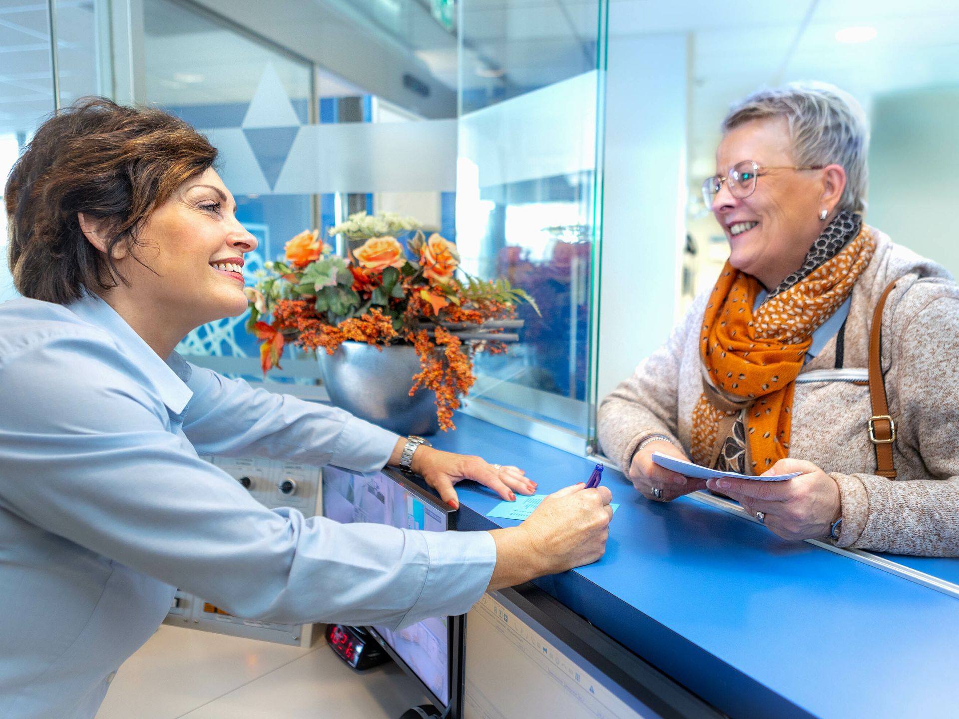 De receptioniste van ziekenhuislocatie Refaja praat met iemand aan de balie.