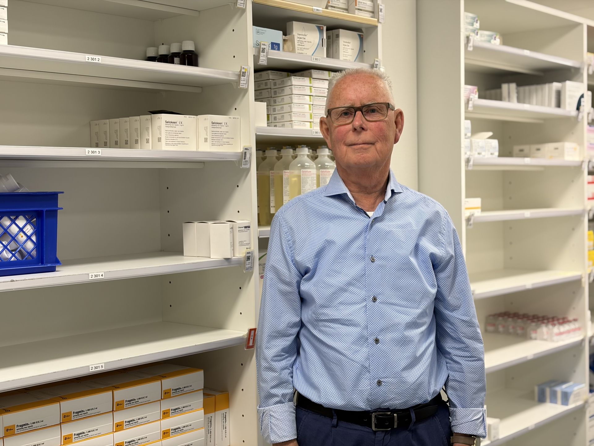 Een man in een apotheek met schappen vol medicijnen.